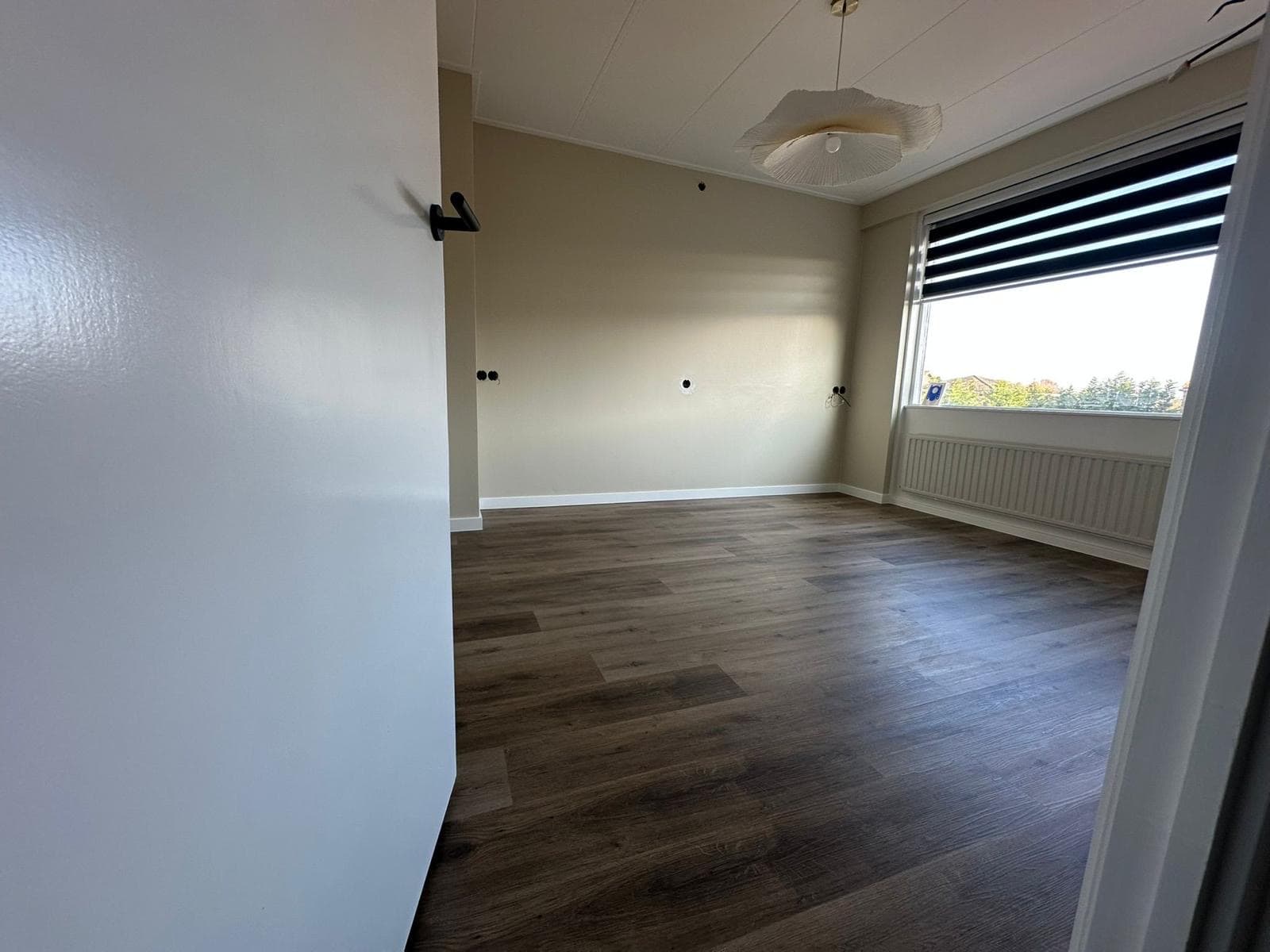 Afgewerkte kamer met donkere houten laminaatvloer, rolgordijn en hanglamp — Vesta Lux project in Zeeland