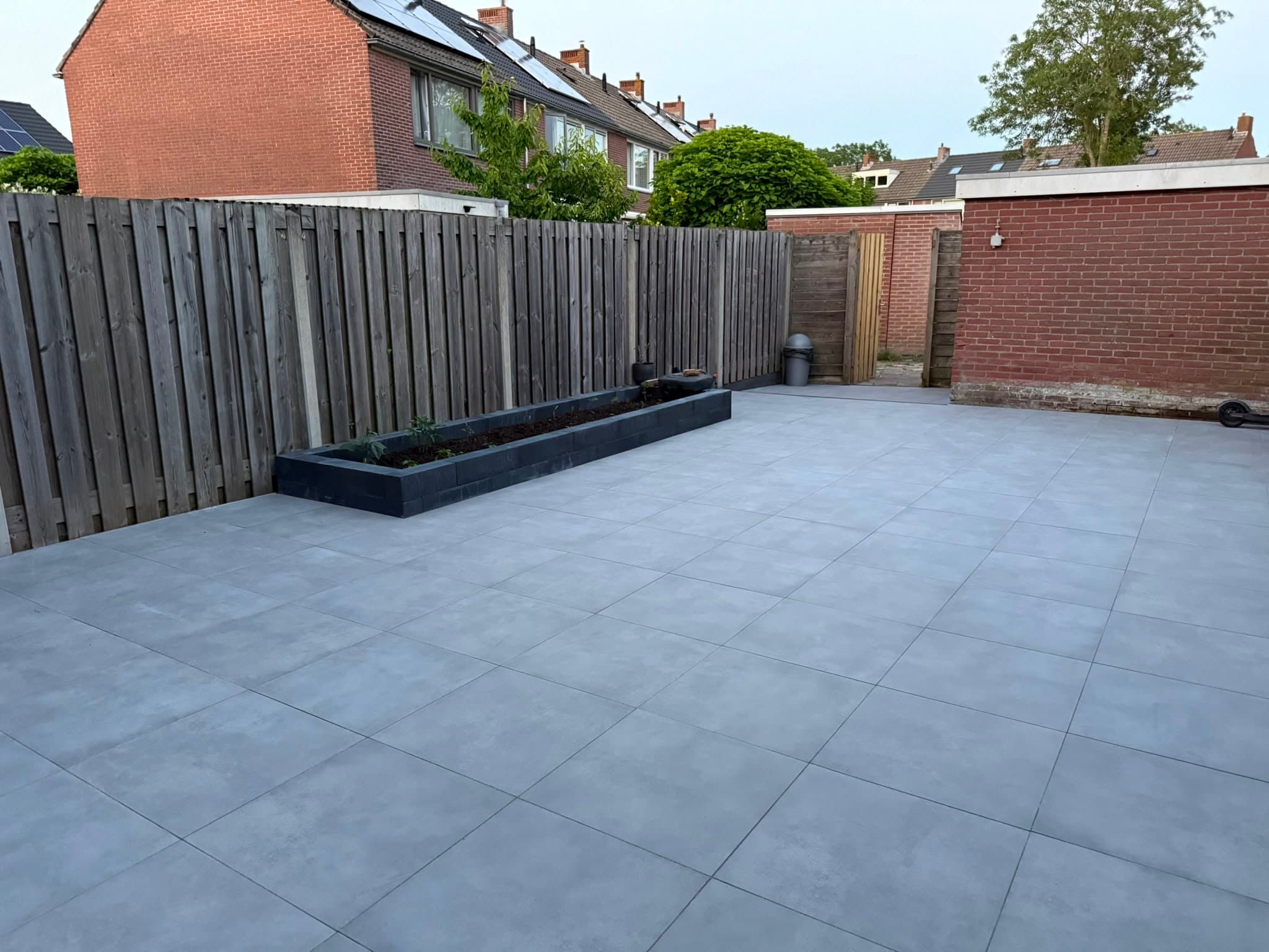 Afgerond terras met grote grijze tegels, houten schutting en een verhoogde zwarte plantenbak — Vesta Lux project in Zeeland