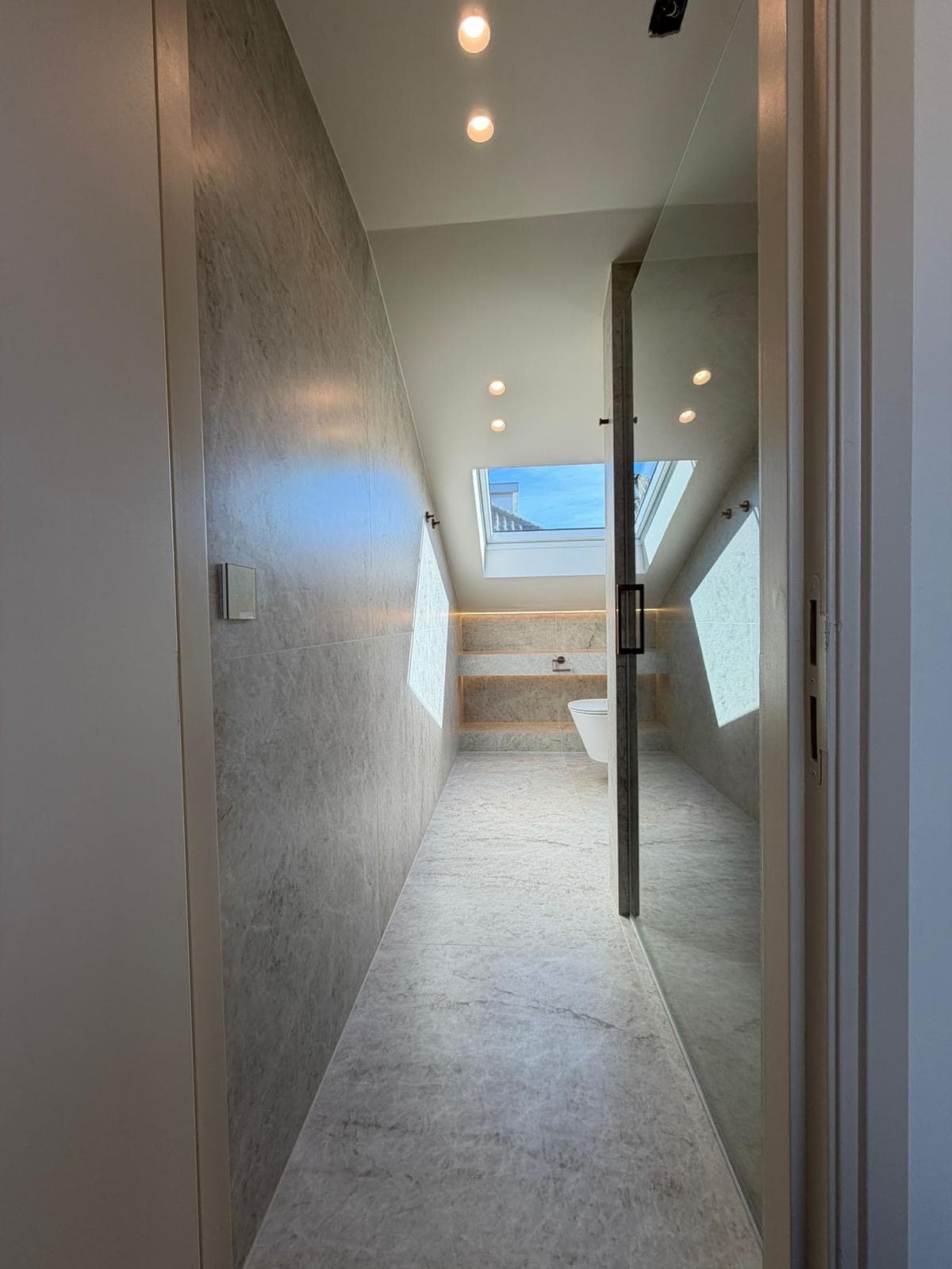 Zolderbadkamer met schuine wanden, marmerlook tegels en een dakraam met uitzicht — Vesta Lux project in Zeeland