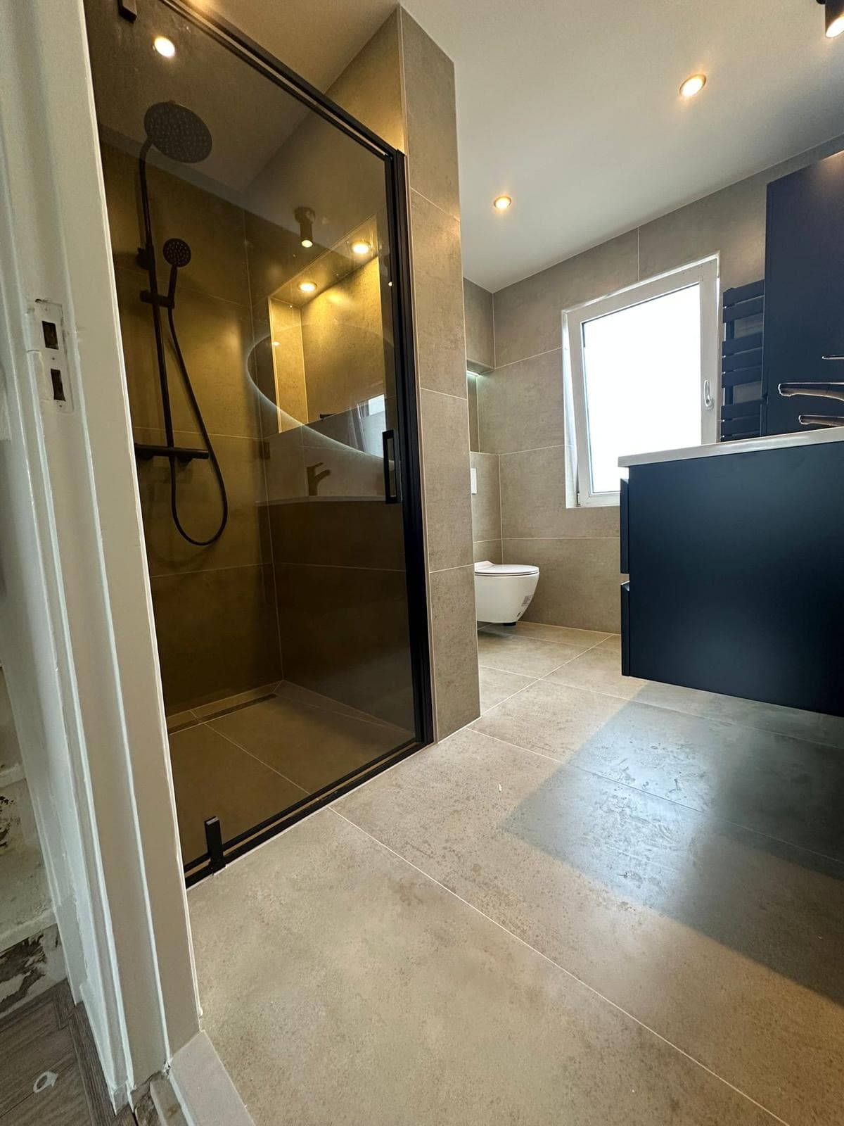Badkamer met gerookt-glazen douchehoek, hangend toilet en een donker wastafelmeubel — Vesta Lux project in Zeeland